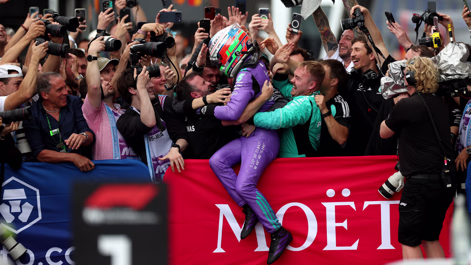 Kimi Antonelli celebrating his 2026 Miami Grand Prix win with the Mercedes team, jumping into a crowd of mechanics behind a red Moët & Chandon banner.