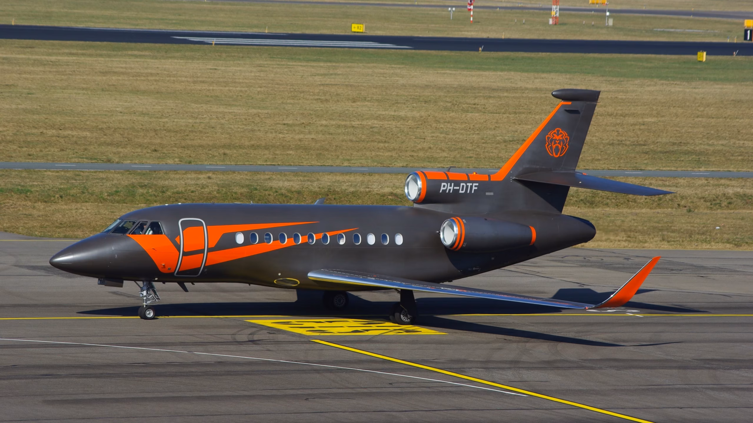 Max Verstappen's custom matt black and orange Dassault Falcon 900EX private jet taxiing on the tarmac.
